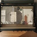 Otevřený černý kufřík s vnitřním mechanizmem páskového ozvěnařu. V plastovém pouzdře jsou dva papíry s nápisy ECHO CHAMBER TAPE RT-1L a návod v obráz…