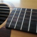 Detailní pohled na hmatník akustické kytary s kovovými pražci a nylonovými strunami. Hmatník je vyroben z tmavého dřeva, korpus kytary je světlý s vi…