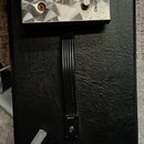 Černý kytarový pedál s kovovou horní deskou. Na desce jsou dva spínače a nápisy ENGL, Tube Amp, FOOTPEDAL Z-4 a u spínačů ON/OFF. Povrch kovové desky…