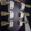 Záběr na zadní stranu hlavy kytary v černé barvě. V horní části je nápis Vintage a John Hornby Skewes Product® a pod ním logo Vintage s textem Design…