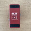 Spodní strana červeného efekt pedálu z kovu. Uprostřed je bílý štítek s nápisy NUX, www.nuxefx.com, AC ADAPTER: DC 9V, CE, symbol přeškrtnuté popelni…