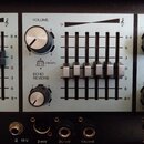 Detailní pohled na ovládací panel elektronického zařízení s modrými sekcemi. Jsou zde vidět posuvníky, otočné knoflíky a nápisy VOLUME, VIBRATO, ECHO…