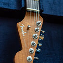 Detail hlavy elektrické kytary z dřeva s přirozeným povrchem. Na hlavě je bílý nápis "Fender" a pod ním menší text "STRATOCASTER". Jsou vidět šest ko…