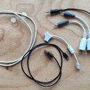 Na dřevěném povrchu jsou položeny tři kabely. Bílý kabel má napájecí adaptér s nápisem BEATSTEP PRO v červeném rámečku. Druhý kabel je rozdělovač s č…