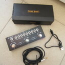 Černý efektový pedál s nápisem M-WAVE a řadou bílých otočných ovladačů. Pod ovladači jsou popisy: VOLUME, IN CAB, REVERB, MIX, FX, TIME, MOD, TONE, G…