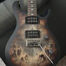 Elektrická kytara s matným povrchem a dřevěnou topovou vrstvou v tmavě hnědé barvě s výraznou strukturou zrzavého dřeva. Nástroj má dva humbuckery, T…