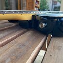 Detailní pohled na spoj hmatníku, krku a těla elektrické kytary. Tělo je černé s vysokým leskem, krk je vyroben ze světlého dřeva. Na boku těla je vi…