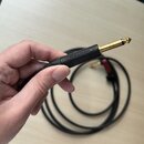 Ruka drží konec černého audio kabelu s pozlaceným 6,3mm jack konektorem. Na černém plastovém pouzdře konektoru je vyraženo logo NEUTRIK. V pozadí je…