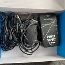 V modré krabici se nachází černý napájecí adaptér a černá napájecí jednotka s nápisy RAZZOR PEDAL, POWER SUPPLY, OUT 18V, OUT 9V (dvakrát) a IN DC 18…