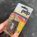 Plastové balení s víceúčelovým nářadím pro bubeníky. Na bílém pozadí obalu je černé logo pdp a nápis DRAUM MULTI-TOOL na barevném pruhu. Uvnitř průhl…