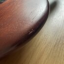 Detailní záběr na hranu hřdelnice dřevěného nástroje v tmavě hnědé barvě. Povrch vykazuje známky opotřebení v podobě drobných škrábanců a odřapání la…