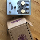Kovový efekt pedál stříbrné barvy s nápisy ORIGIN EFFECTS, MAGMA57 a CLASSIC AMP OVERDRIVE • TRUE PITCH MODULATION. Zařízení má dva stomečovací spína…