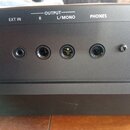 Detailní pohled na zadní panel černého elektronického zařízení. Jsou zde vidět konektory s nápisy EXT IN, R, L/MONO a PHONES, přičemž konektory R a L…
