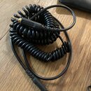 Černý spirálový kabel s konektory typu jack na obou koncích. Na plastovém krytu jednoho z konektorů je vyryt nápis MADE IN CHINA. Kabel je položen na…