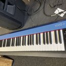 Modré digitální piano s bílými a černými klávesami. Na horní liště je vpravo nápis VIVO S1 a vlevo nápis DXBELL. V pravém ovládacím panelu jsou tlačí…