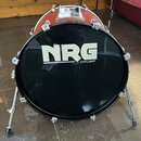 Černý basový buben s červeným korpusem, umístěný na kovovém stojanu. Na předním černém koženu je bílý nápis NRG DRUMS. Povrch nástroje vykazuje mírné…