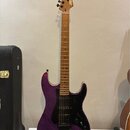 Fialová elektrická kytara s tmavým hmatníkem a černým pickguardem. Na hlavě je viditelné zlaté logo „Squier“. Tělo má lakovaný povrch s viditelnou st…