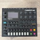 Černý digitální syntetizátor s nápisem Elektron v pravém horním rohu. Zařízení obsahuje displej s textem Polyphonic Digital Synthesizer a Digitone, n…