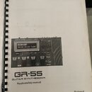Fotografie znázorňuje kroužkový vázaný uživatelský manuál. Na bílém povrchu je obrázek černého přístroje s nápisem Roland GR-55 GUITAR SYNTHESIZER a…