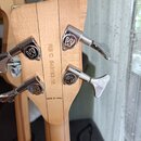 Záběr na zadní stranu hlavy basové kytary z přírodního světlého dřeva. Na dřevě je vyryto RB C 543183-16 a nápis MADE IN CHINA. Nástroj má tři chromo…