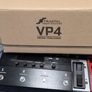 Kartonová krabice s nápisy FRACTAL AUDIO SYSTEMS, VP4 a VIRTUAL PEDALBOARD. Pod krabicí je umístěno černé zařízení s kovovým povrchem, které má čtyři…
