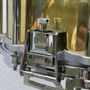 Detailní záběr na chromovaný mechanismus pedálu u mosazného bubnu zlaté barvy. Na kovovém krytu je vyryto logo Pearl. Povrch mosazi vykazuje drobné š…