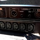 Detail zadní strany dvou černých rackových zařízení. Horní přístroj má nápisy CHANNEL 1, OUTPUT a INPUT u konektorů XLR a jack. Spodní přístroj obsah…