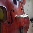 Detailní pohled na tělo smyčcového nástroje, pravděpodobně kontrabasu, s tmavě hnědým lakovaným povrchem. Na nástroji je vidět světle barevný dřevěný…