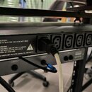Černý rackový rozvodč rač s řadou šesti zásuvek. Na levé straně je vypínač a vstup AC IN, nad ním značka CE. Na přístroji je bílý varovný text: CAUTI…