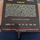 Fotografie zachycuje zadní stranu černého obalu na basové struny. Je zde uveden název HI-BEAMS™, nápis MADE IN U.S.A. a text popisující vlastnosti st…