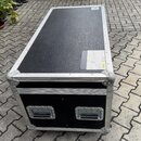 Černý transportní flightcase s hliníkovými hranami a kovovými rohy. Na přední straně jsou dvě černé plastové madla s kovovým rámem. Povrch je z textu…