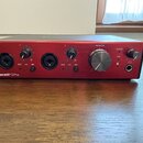 Červený audio rozhraní s kovovým povrchem a stříbrným ovládacím knoflíkem MONITOR. Na předním panelu jsou dva kombinované vstupy, čtyři menší knoflík…
