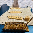 Modrá elektrická kytara s bílým perleťovým pickguardem a zlatým hardwarem. Na snímači je nápis R.M.pickups. Viditelný zlatý kobylník a knoflík s nápi…