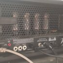 Zadní strana černého kytarového zesilovače s kovovou mřížkou, skrze kterou jsou vidět čtyři elektronky. Na spodním panelu je nápis Peavey a řada kone…