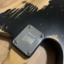 Detail zadní strany krku elektrické kytary s černým lakem, který je v horní části výrazně odloupaný a od reveals světlé dřevo. Na krku je přišroubova…