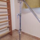 Stříbrný kovový stativ s teleskopickým mechanismem a třemi utahovacími šrouby. Horní část stativu je připojena k šikmé kovové tyči. Povrch vykazuje m…