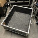Otevřený transportní kufřík s černým povrchem a hliníkovými hranami. Vnitřek je vyložen šedým plstěným materiálem. Na přední straně je umístena černá…