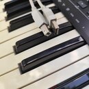 Detailní záběr na klávesy elektronického klavíru s černými a bílými klávesami. Na klávesách leží dva šedé kabely s konektory. V pravém horním rohu je…
