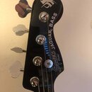 Fotografie zachycuje hlavu černého basového nástroje se čtyřmi chromovanými ladičkami. Na povrchu je bílý nápis Squier by Fender JAGUAR BASS a v horn…