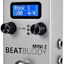 Stříbrný efekt pedál s nápisem BEATBUDDY MINI 2. Zařízení má modrý displej s textem Rock 1, 100 a 4/4, dva černé ovládací knoflíky u nápisu VOLUME a…