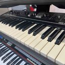 Detailní pohled na klávesnice dvou elektronických klavírů umístěných nad sebou. Horní nástroj je černé barvy s nápisem Roland a viditelnými ovládacím…