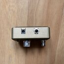 Fotografie zachycuje zadní stranu efekt pedálu v matné zlatavé barvě. Na zadním panelu jsou umístěny dva konektory: napájecí vstup a jackový výstup.…