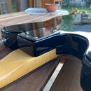 Detail zadní části černé elektrické kytary v místě spoje krku s tělem. Na černém lakovaném povrchu je vidět kovový kryt s nápisem SURGE. Lak vykazuje…