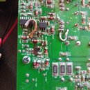 Fotografie detailu zelené printed board s elektronickými součástkami. Na desce jsou viditelné stopy po opalení, zoxidované kontakty a několik volně v…