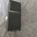 Černý kytarový pedál s povrchem potaženým černou texturou připomínající tkaninu. Zařízení má obdélníkový tvar a na levé straně je viditelný kovový sp…