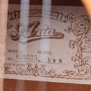 Fotografie znázorňuje vnitřní štítek kytary s ornamentálním rámem. Uprostřed je výrazné logo Aria a nápis Fine Quality Guitars. Štítek obsahuje údaje…