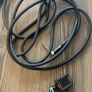 Černý audio kabel s nápisem Roland Professional Audio Cable a konektorem značky Roland. Vedle kabelu je umístěn malý černý digitální tuner s logem JO…
