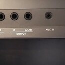Detail zadního panelu šedého elektronického zařízení s řadou konektorů. Jsou zde nápisy 16V, FOOT PEDAL s čísly 1 a 2, OUTPUT s označením R a L/L+R,…