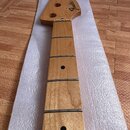 Dřevěný krk elektrické basy s hmatníkem z jednoho kusu dřeva a kovovými pražci. Na hlavě je černý nápis Fender a menší text JAZZ BASS. V hmatníku jso…