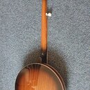 Zadní pohled na banjo s hnědým lakovaným povrchem v přechodovém odstínu. Na zadní straně hlavy je bílý štítek s nápisy "MADE IN CHINA" a "CE". Nástro…